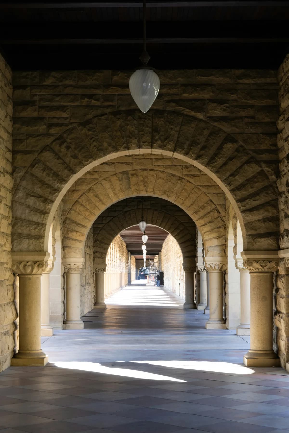 A sunlit sandstone arcade with repeating arches leading towards open daylight